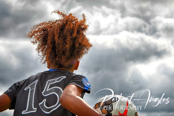 Youth soccer player with curly hair against cloudy sky